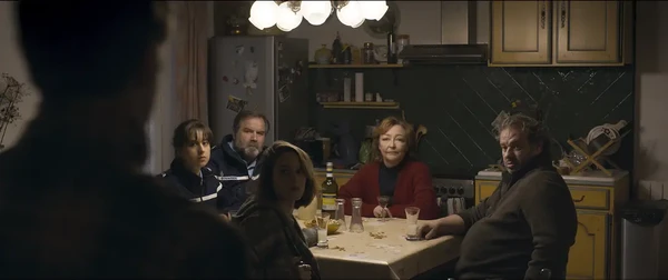 Characters gather around a table in a tense family - like scene in "Miséricorde".