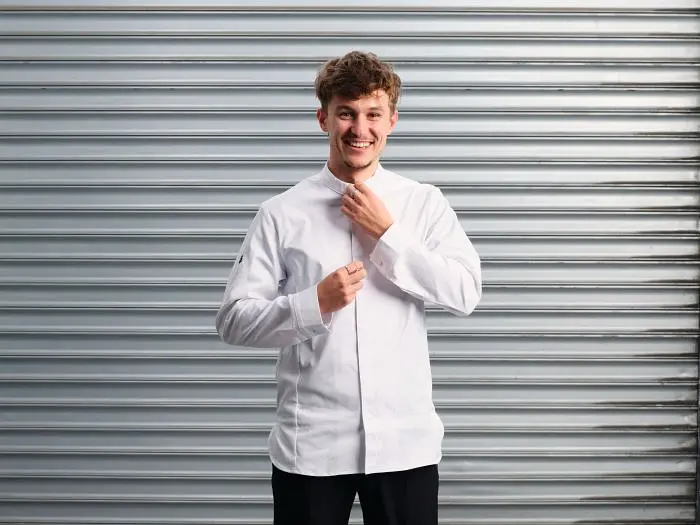 A young chef adjusts his coat, smiling in "Top Chef France".